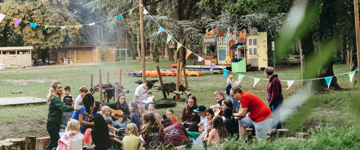 groep jongeren en volwassenen rond kampvuur in open lucht