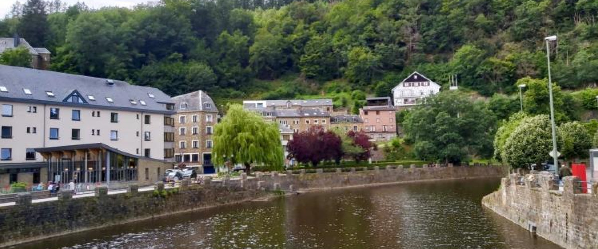 brede rivier met aan de zijkant gebouwen en bossen op de heuvelachtige achtergrond